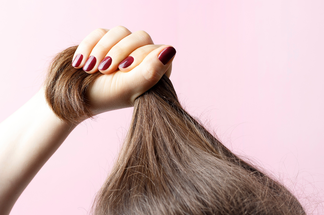 Nahmanufnahme Hand mit rot lackierten Nägel hält Haare fest vor rosa Hintergrund